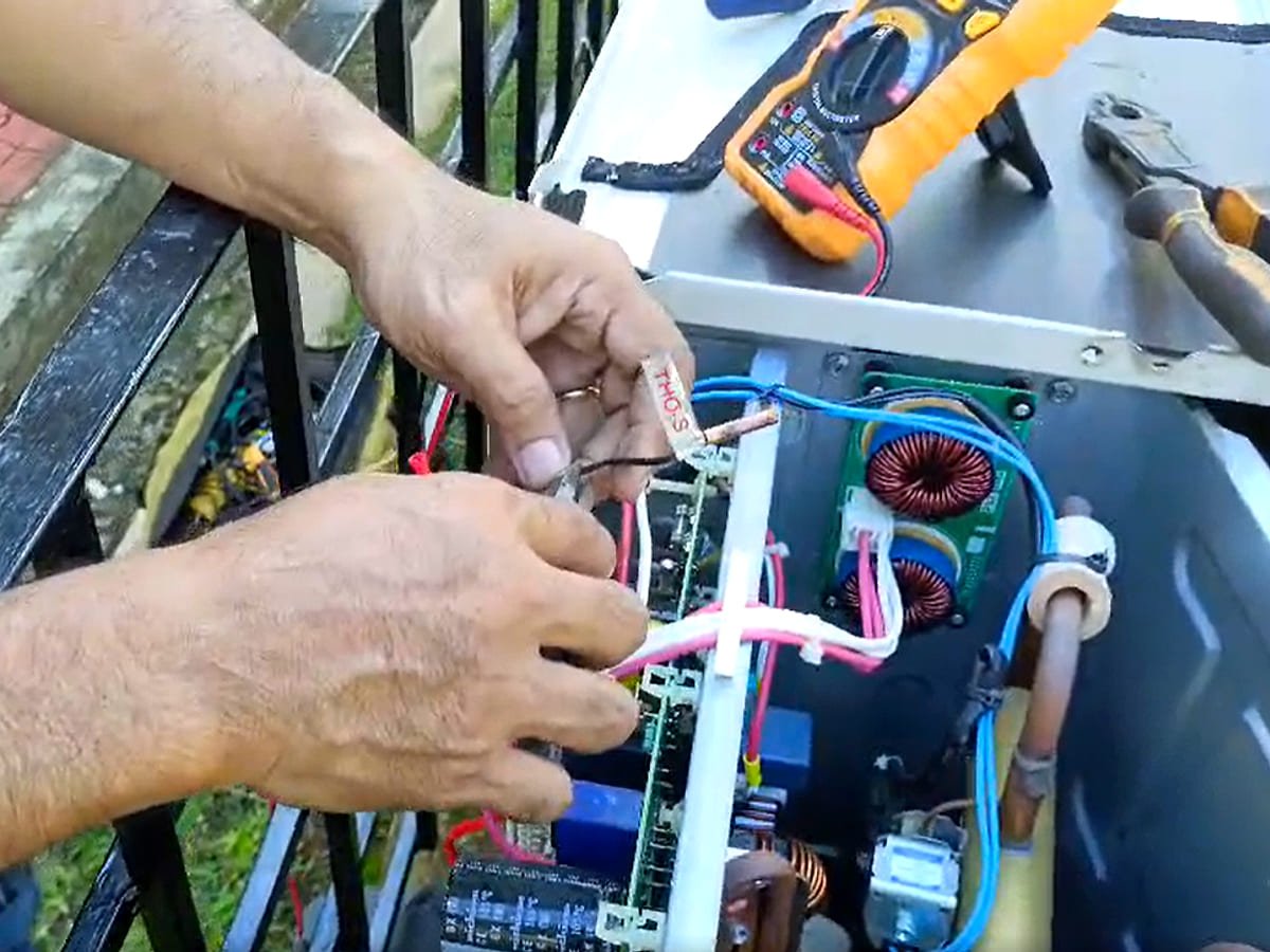 Technician tracing a fault on an inverter control board with a multimeter and hand tools alongside